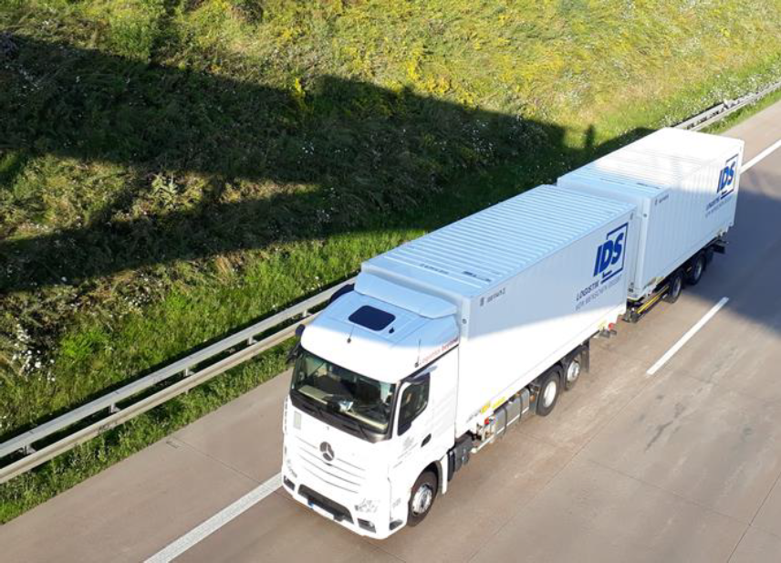 White semitrailer truck on highway next to green area in sunshine.