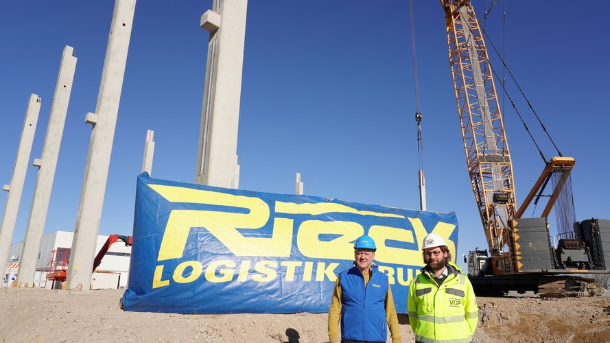2 construction workers in front of the Rieck logo next to the excavator