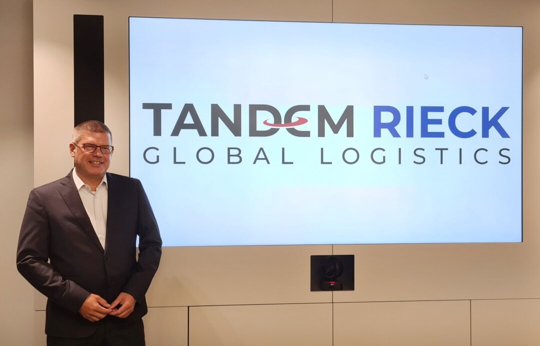 Das Bild zeigt einen Mann, der vor dem Logo von Tandem Rieck steht.