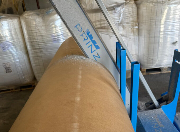 Große Papierrolle auf einer blauen Maschine in einer Lagerhalle.