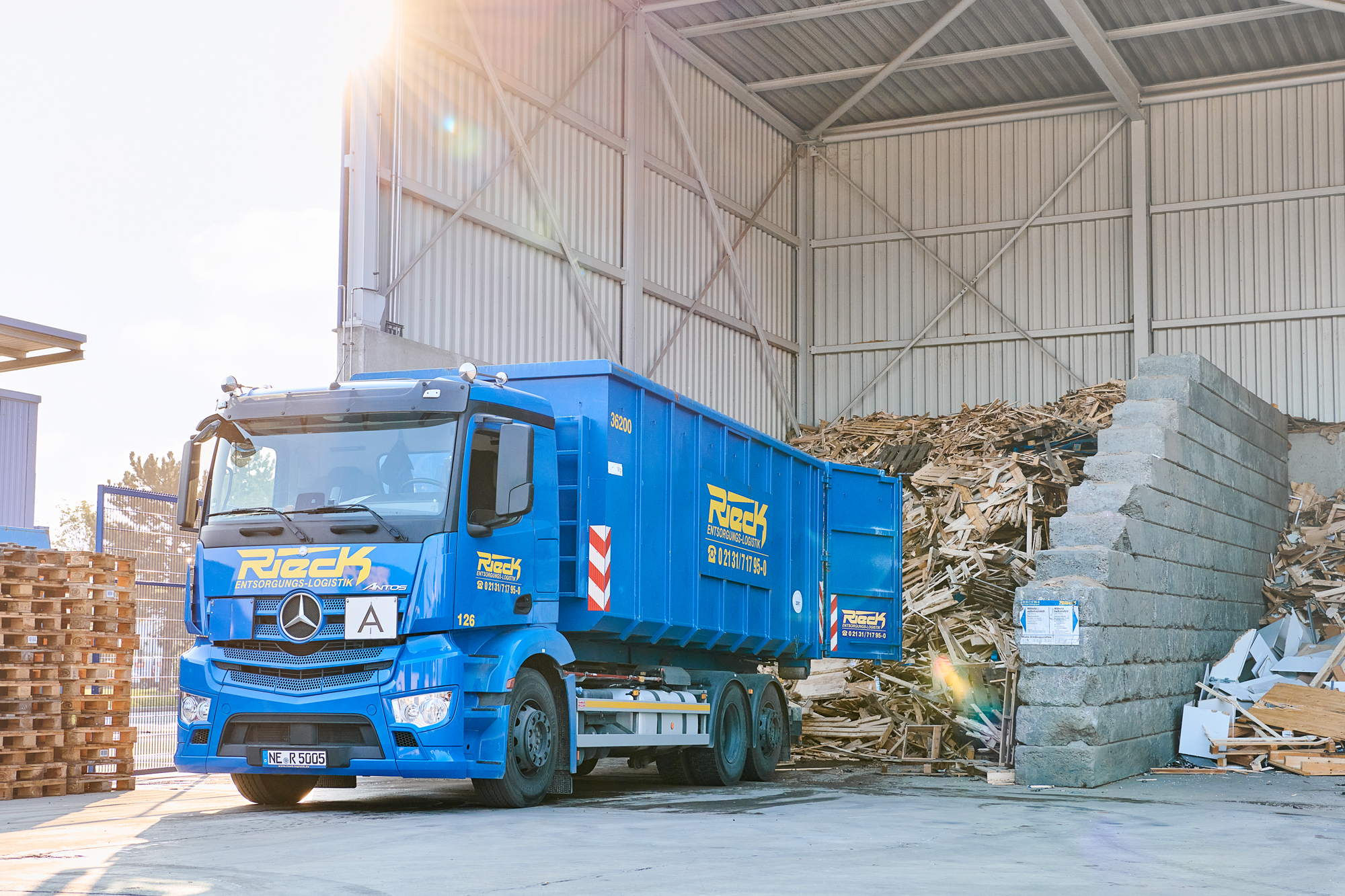 Blauer LKW in einer Halle neben einem großen Haufen Holzabfällen.