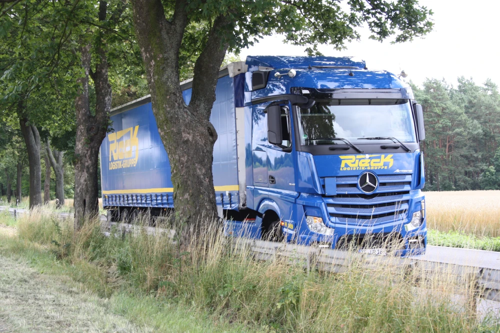 Blue truck with trailer on country road, surrounded by trees and fields.