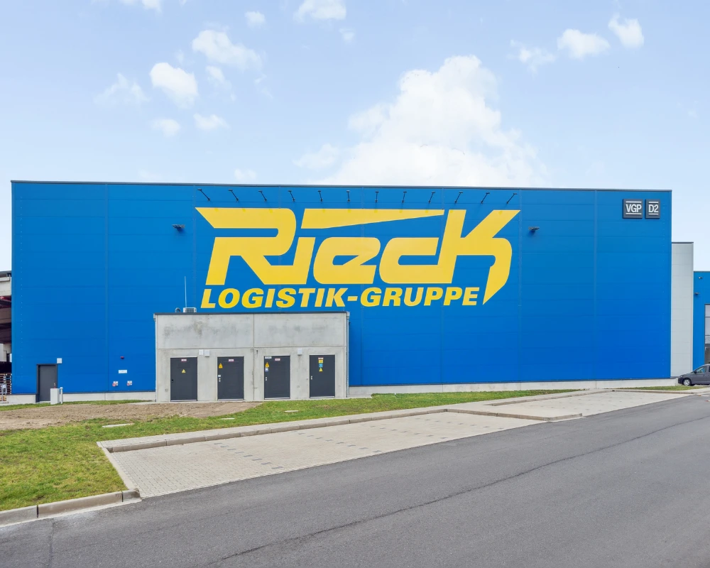 Großes blaues Lagergebäude mit gelbem Schriftzug Rieck Logistik-Gruppe.