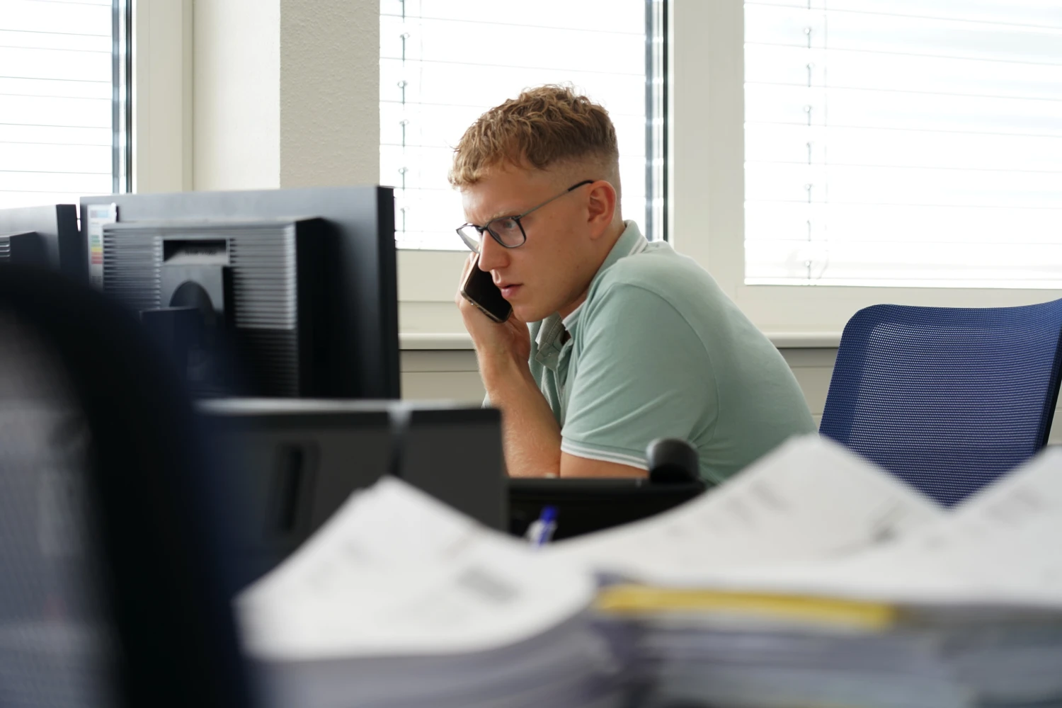 Junger Mann mit Brille spricht am Telefon in einem Büro.