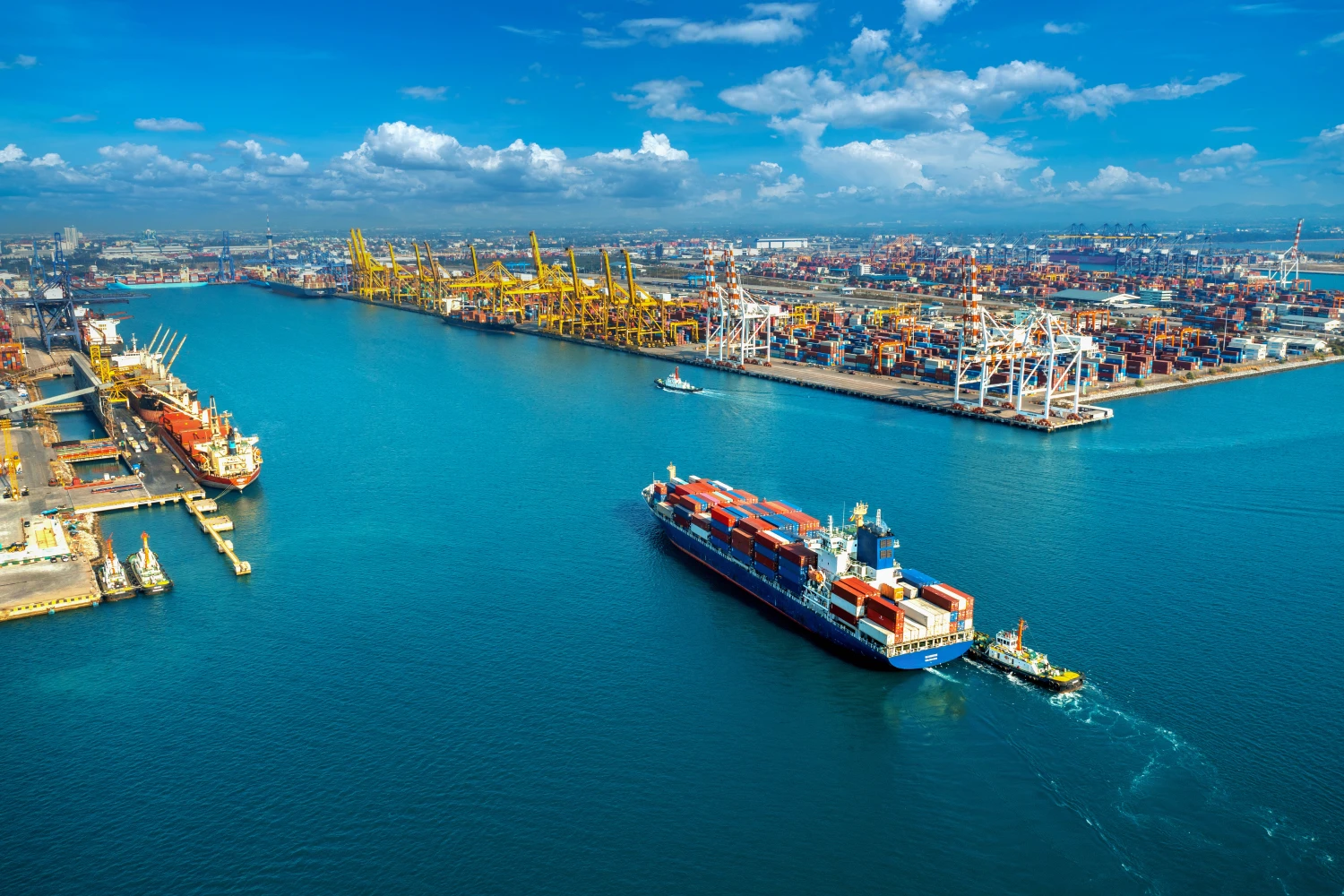 Large container port with several cargo ships and numerous containers under a blue sky.