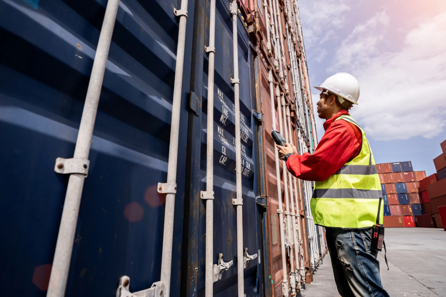 Arbeiter mit Schutzhelm und Warnweste überprüft Container an einem Hafen.