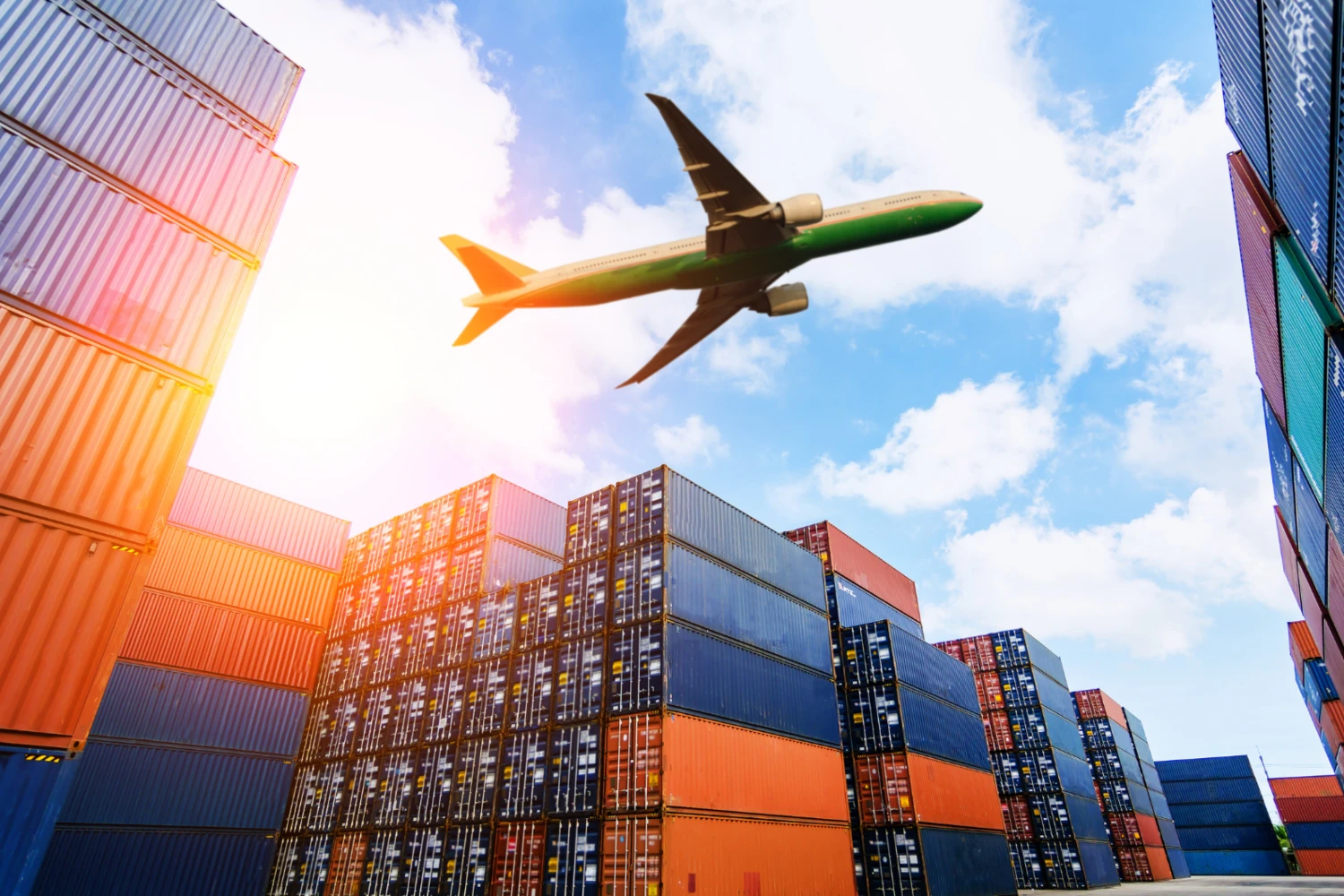 Flugzeug fliegt über bunte Container im Hafen bei sonnigem Himmel.