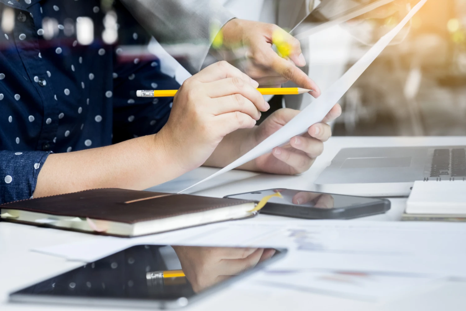 Person hält Stift und Tablet, arbeitet an Dokumenten am Schreibtisch mit Smartphone und Notizbuch.
