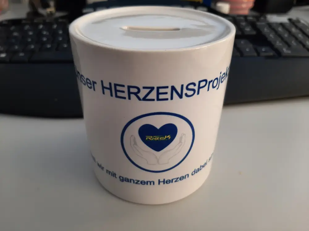 Spendenbüchse mit Aufschrift "Herzensprojekt" und Herzsymbol auf einem Schreibtisch.