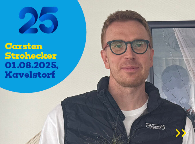 Mann mit Brille und Weste vor Wand mit Text zu 25 Jahren Carsten Strohecker, 01.08.2025, Kavelstorf.