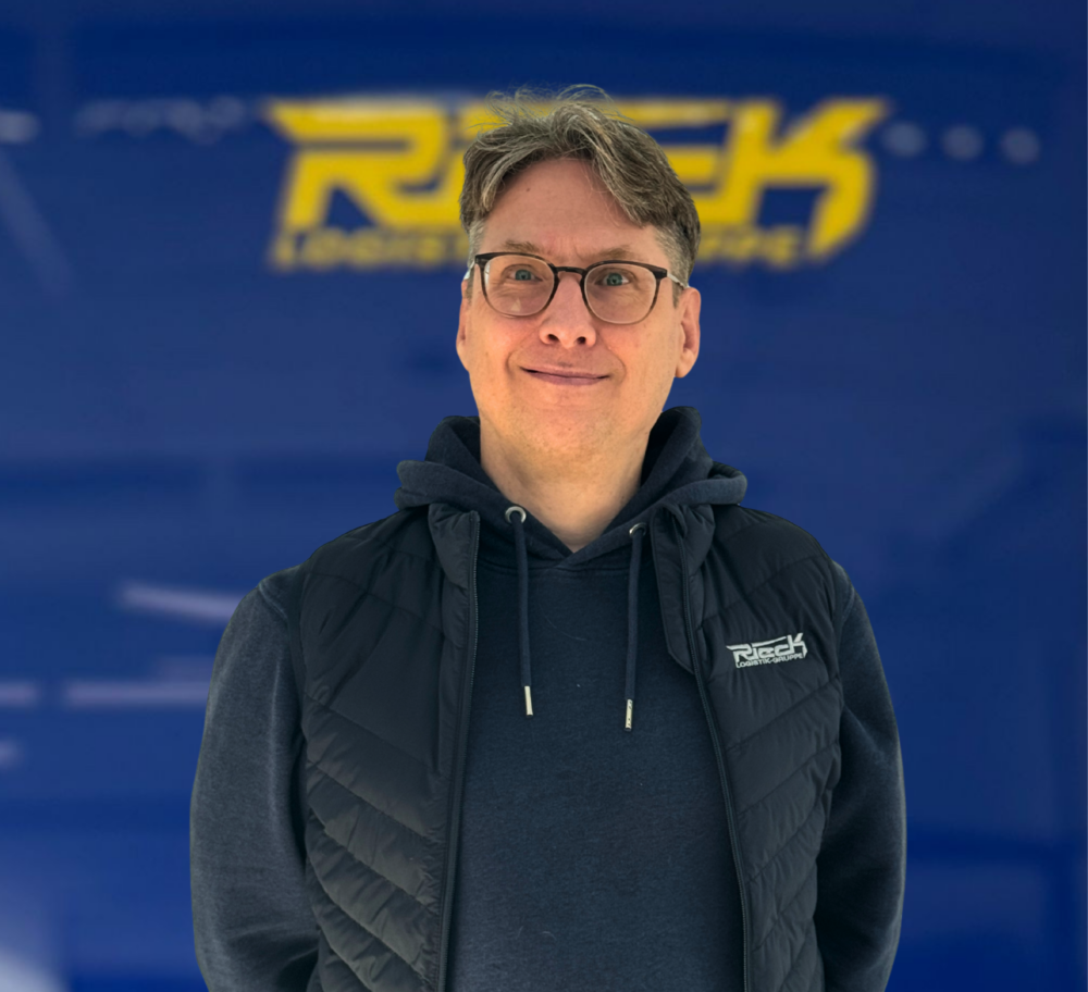 Mann mit Brille und dunkler Jacke vor blauem Hintergrund mit gelbem Schriftzug